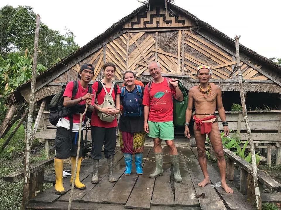 Travelers and a local host in front of an Uma longhouse